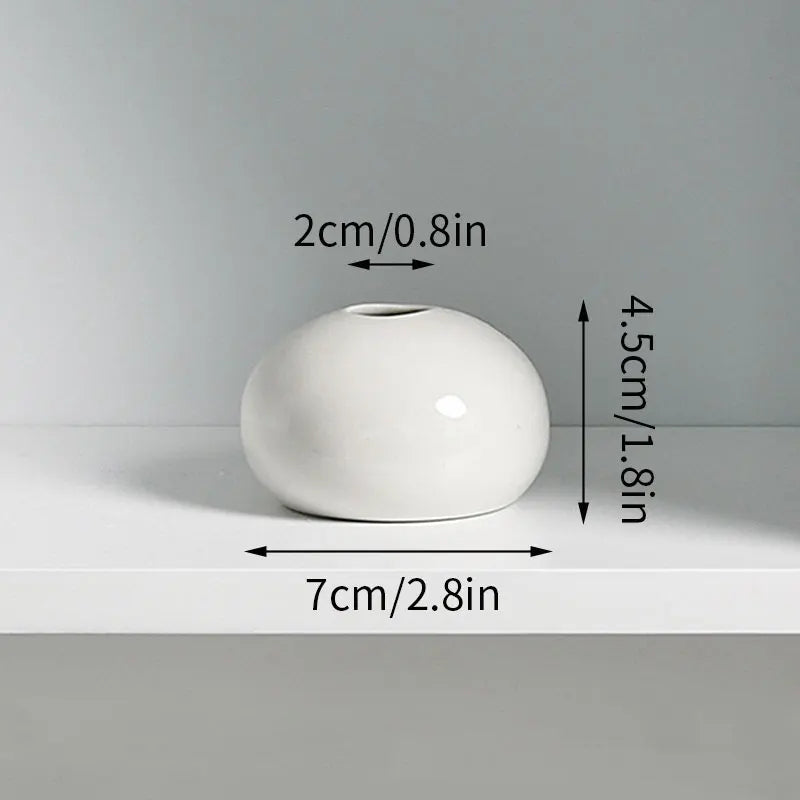 A white ceramic mini vase with a smooth, rounded shape is shown on a light surface.