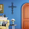A dark metal cross wall decor is mounted on a blue wall next to a wooden door and a yellow sofa.