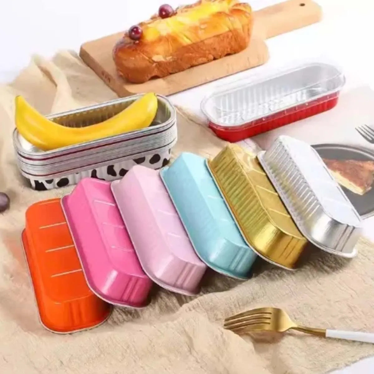 A set of mini foil bread trays and containers in various colors like yellow, pink, blue, and gold are displayed on a beige cl