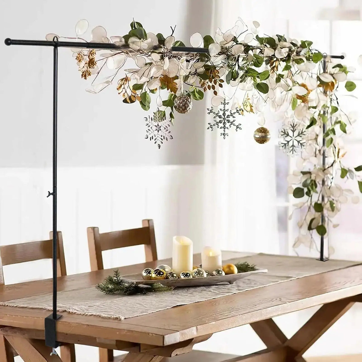 An adjustable balloon arch stand with clamps displaying a floral and greenery arrangement above a wooden table.