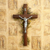 A handcrafted wooden cross with a silver crucifix and dried floral wreath mounted on a textured parchment background.