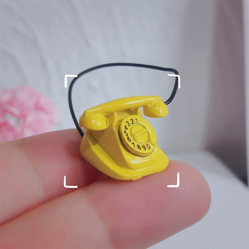 A yellow vintage rotary desk phone miniature decor is held between fingers against a light background.