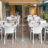 An outdoor dining area set up with white tables and chairs under a beige canopy.