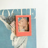 A close-up of a pink magnetic photo frame displaying a woman's face against a teal background.