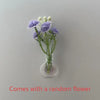 A small glass vase holds a sprig of purple and white flowers on a light gray background.