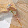 A single realistic white artificial rose with green leaves is displayed on a light brown box and translucent fabric.
