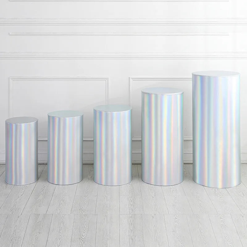 A row of five silver iridescent spandex cylinder stands displayed against a white wall.