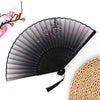 A black vintage bamboo folding fan with sheer fabric and pink floral accents is shown next to a woven straw mat.