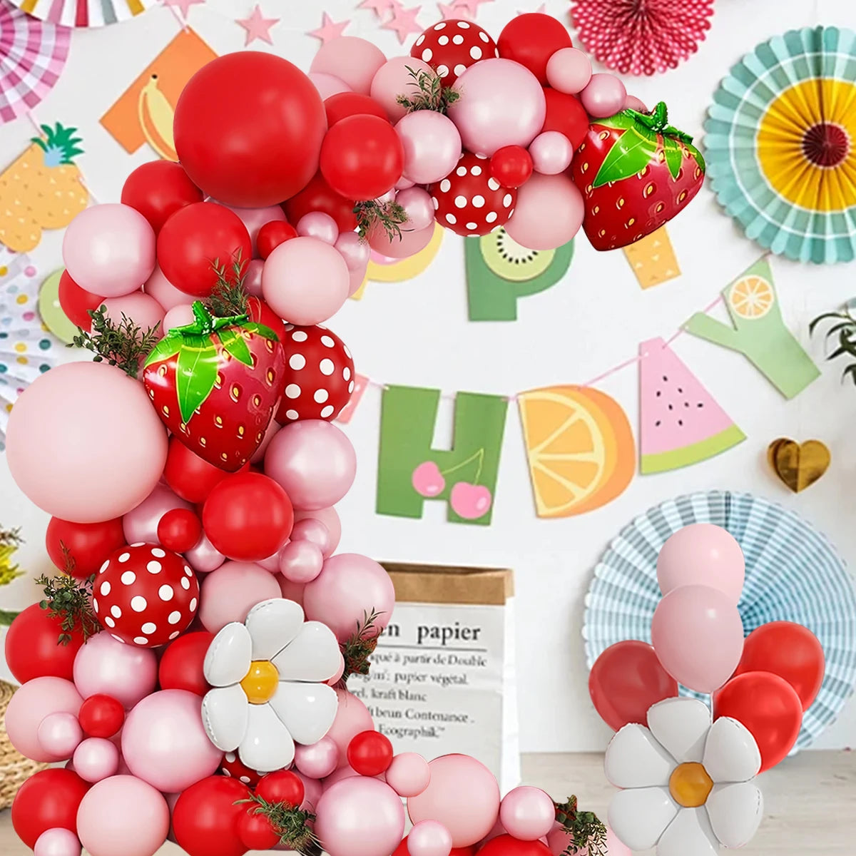 A vibrant pink and red balloon arch wreath kit featuring strawberries and fruit accents.