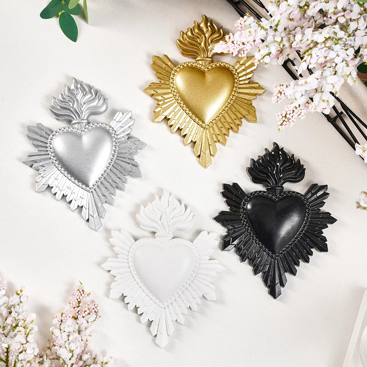 A collection of three heart-shaped resin wall decorations in gold, silver, and black, surrounded by pink flowers.