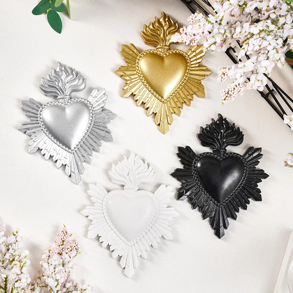 A collection of three heart-shaped resin wall decorations in gold, silver, and black, surrounded by pink flowers.