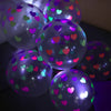 Ein Cluster leuchtender Latexballons mit mehrfarbigen Herzen, beleuchtet vor dunklem Hintergrund.