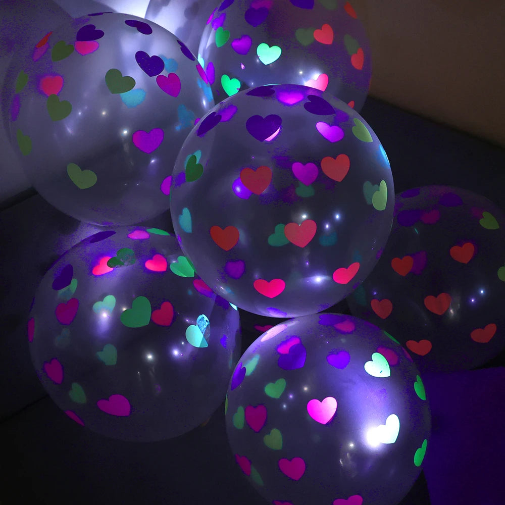 Ein Cluster leuchtender Latexballons mit mehrfarbigen Herzen, beleuchtet vor dunklem Hintergrund.