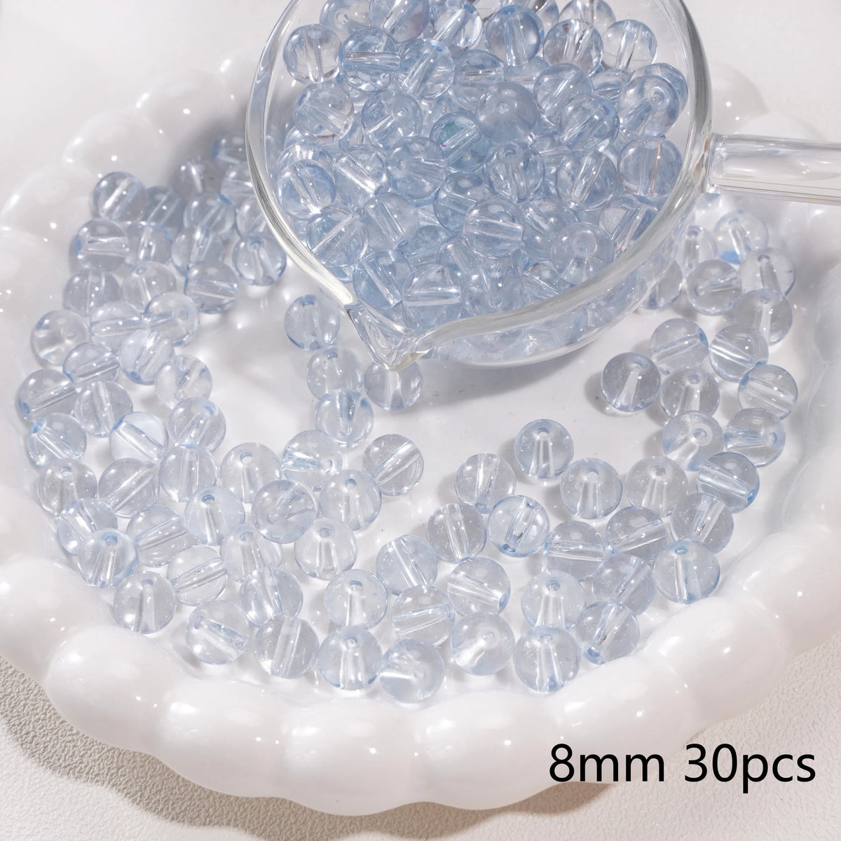 A clear glass dropper filled with small light blue spacer beads resting on a white dish.