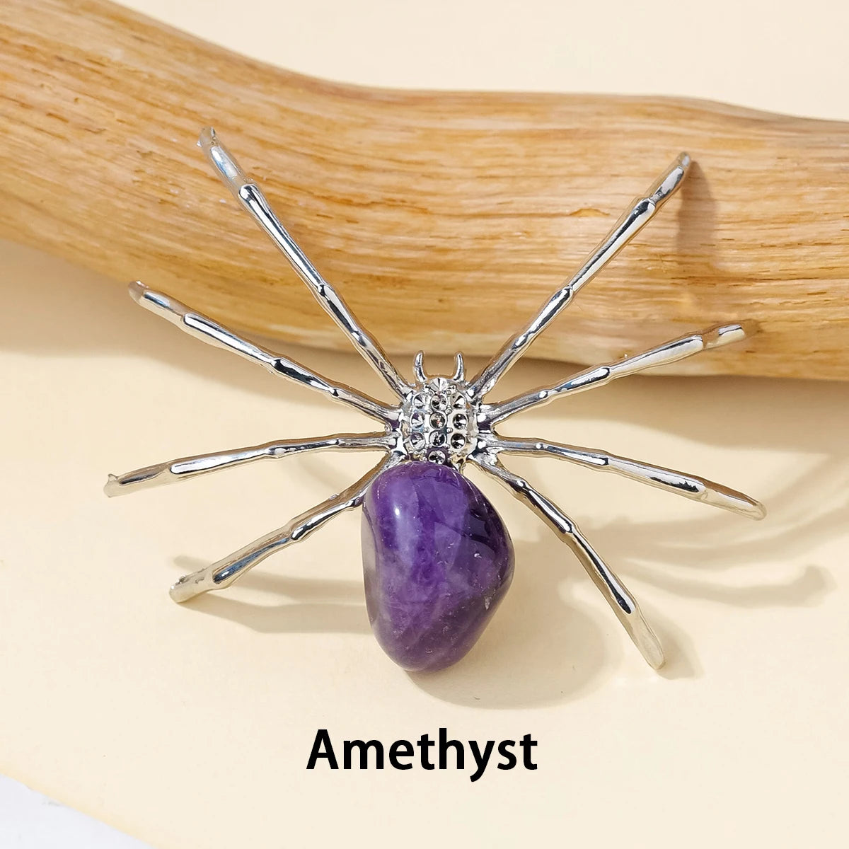 A handcrafted crystal spider figurine with silver legs and a purple amethyst body resting on a wooden surface.