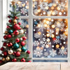 A decorated Christmas tree stands in front of a window featuring snowflake window clings and bokeh lights.