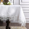White embroidered lace tablecloth with floral pattern and delicate lace trim on a dark pedestal table.