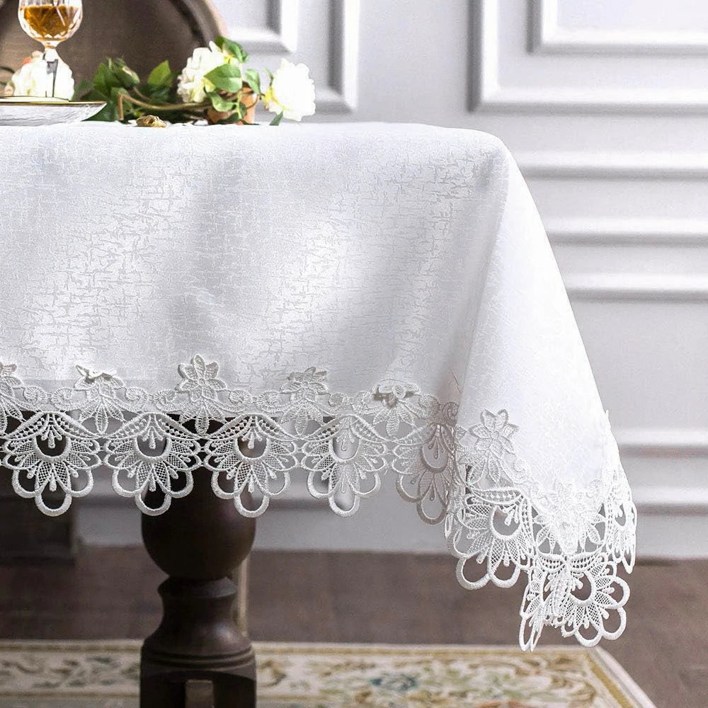 White embroidered lace tablecloth with floral pattern and delicate lace trim on a dark pedestal table.