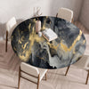 A round table set for dining featuring a marble print tablecloth with gold veining on a dark background.