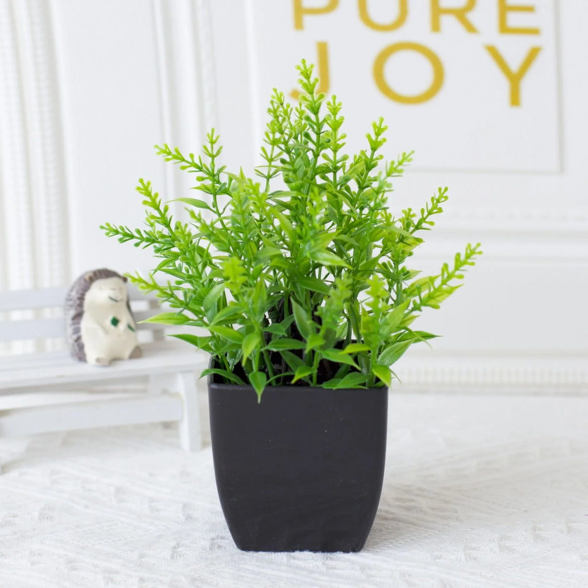 A potted green artificial eucalyptus plant sits on a white surface next to a small ceramic animal.