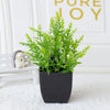 A potted green artificial eucalyptus plant sits on a white surface next to a small ceramic animal.