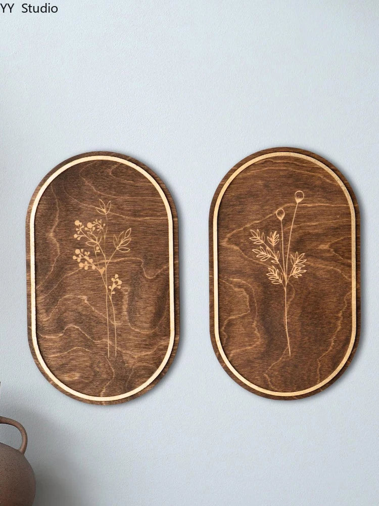 A pair of oval wooden wall decor pieces featuring delicate botanical line drawings on dark wood with natural edge finishing.