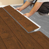 A person is applying wood grain self-adhesive decals to a floor, showing the texture and installation process.