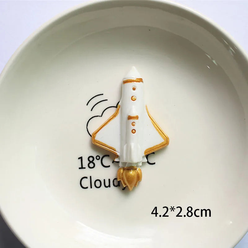 Décoration de gâteau d'astronaute miniature blanche avec accents dorés sur une assiette blanche.