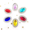 A collection of flatback rhinestone gemstones in various colors including red, blue, purple, and yellow, scattered on a white