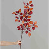 A hand holds a branch of autumn beech simulation leaves with reddish-orange and deep red colors against a gray background.