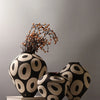 A black and cream ceramic vase with a geometric circle pattern, decorated with dried branches.