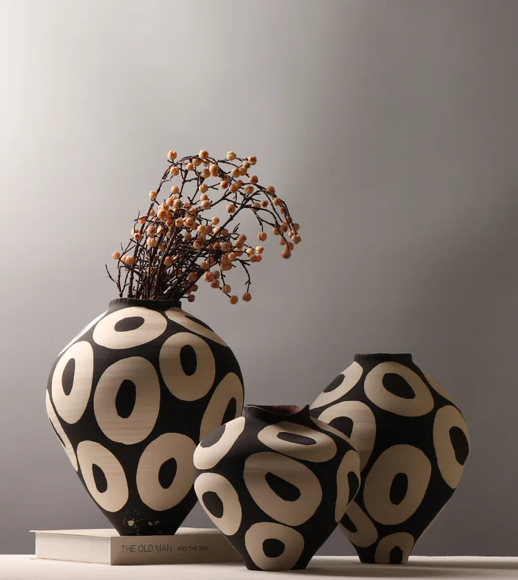 A black and cream ceramic vase with a geometric circle pattern, decorated with dried branches.