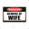 A vintage metal warning sign with a black background and white text that reads WARNING BEWARE OF WIFE.