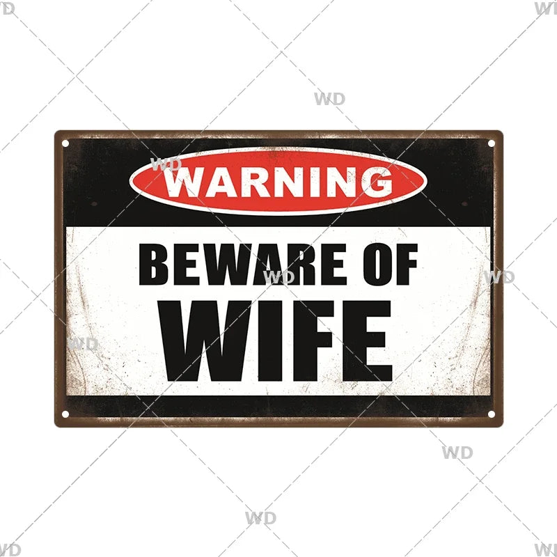 A vintage metal warning sign with a black background and white text that reads WARNING BEWARE OF WIFE.
