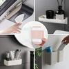 A hand is placing pink reusable double-sided adhesive picture hanging strips into a white storage container on a gray wall.