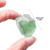 A hand holds a translucent green crystal healing stone, measuring about 3cm long.