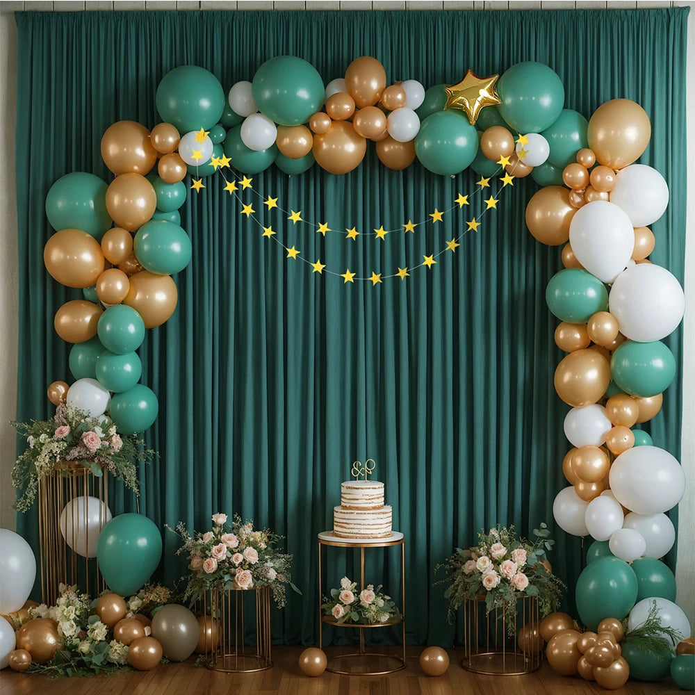 A floral and balloon decorated green backdrop for parties featuring gold and white balloons and greenery.