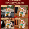 A white ceramic lucky cat ornament with red accents and gold coins sitting on a wooden desk.