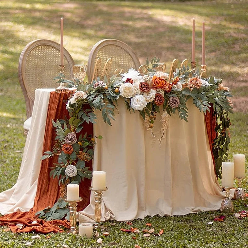 A floral centerpiece display featuring roses and eucalyptus garlands on a draped table for an event.