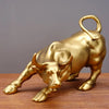 A golden sculpture of a bull with horns and a loop handle, displayed on a wooden surface.