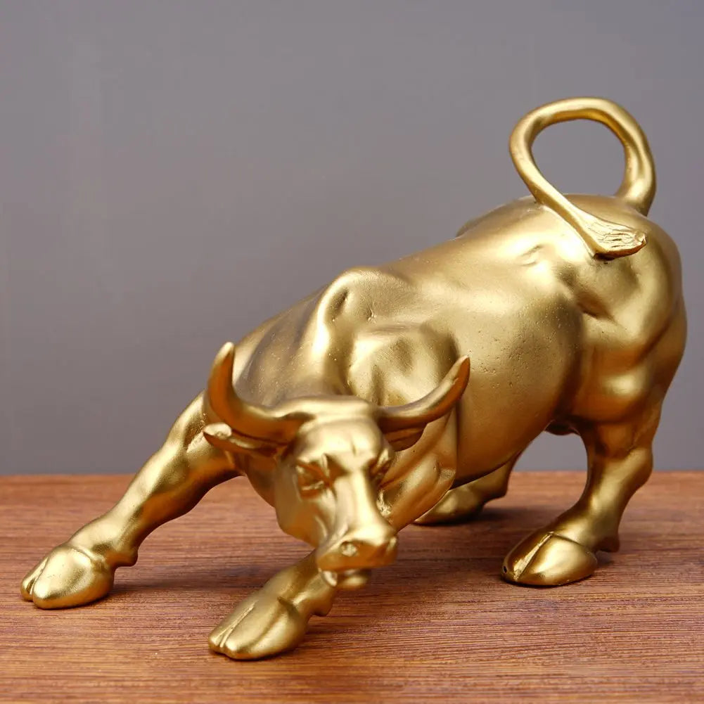 A golden sculpture of a bull with horns and a loop handle, displayed on a wooden surface.