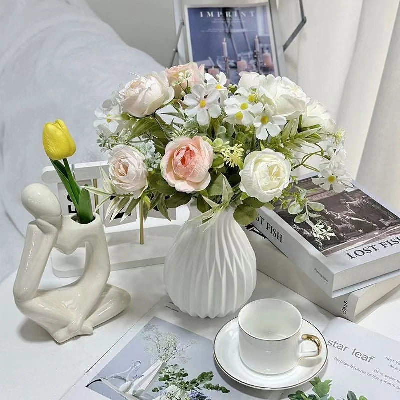 A white ceramic flower vase filled with white and pink flowers sits next to a white sculpture.