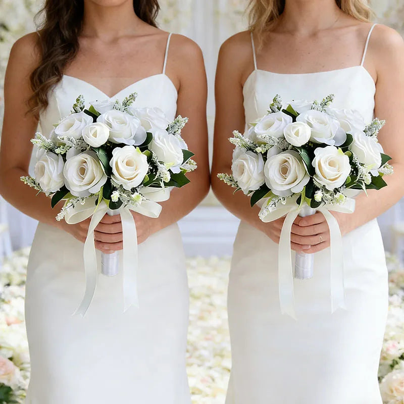 Two brides in white dresses hold elegant bouquets of white roses and greenery.