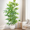 An artificial bamboo branch with green leaves displayed in a white pot on a wooden table next to a light-colored sofa.
