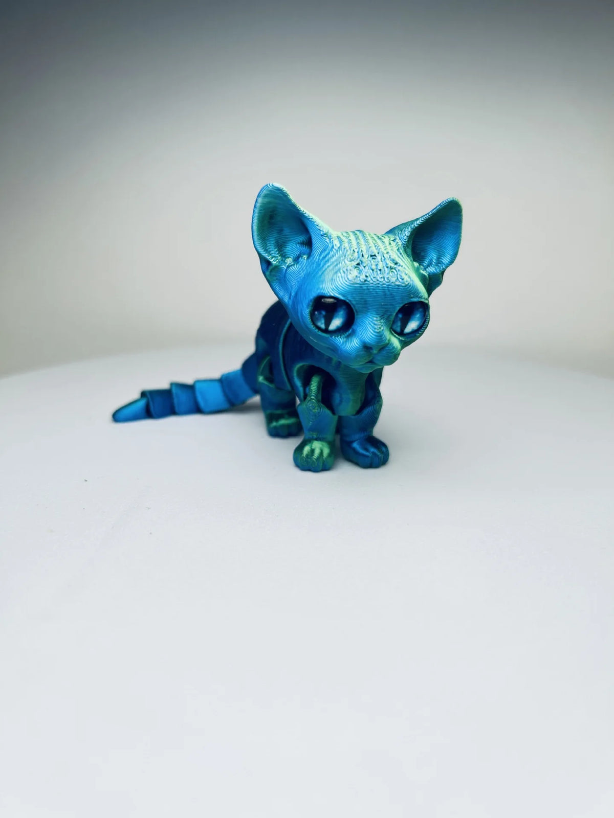 A blue articulated 3D printed figurine of a Siamese cat with large eyes and pointed ears.
