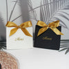 Two elegant paperboard thank you gift bags tied with gold ribbon, set against a light background.