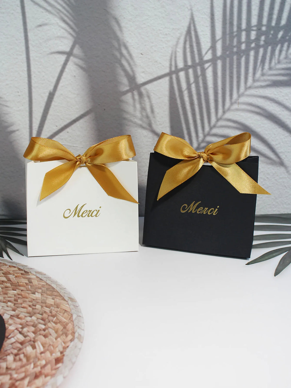 Two elegant paperboard thank you gift bags tied with gold ribbon, set against a light background.