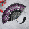 A dark purple and white floral antique folding fan with a black background and a black tassel.