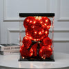 A bright red artificial rose teddy bear displayed in a clear glass jar with warm LED lights.