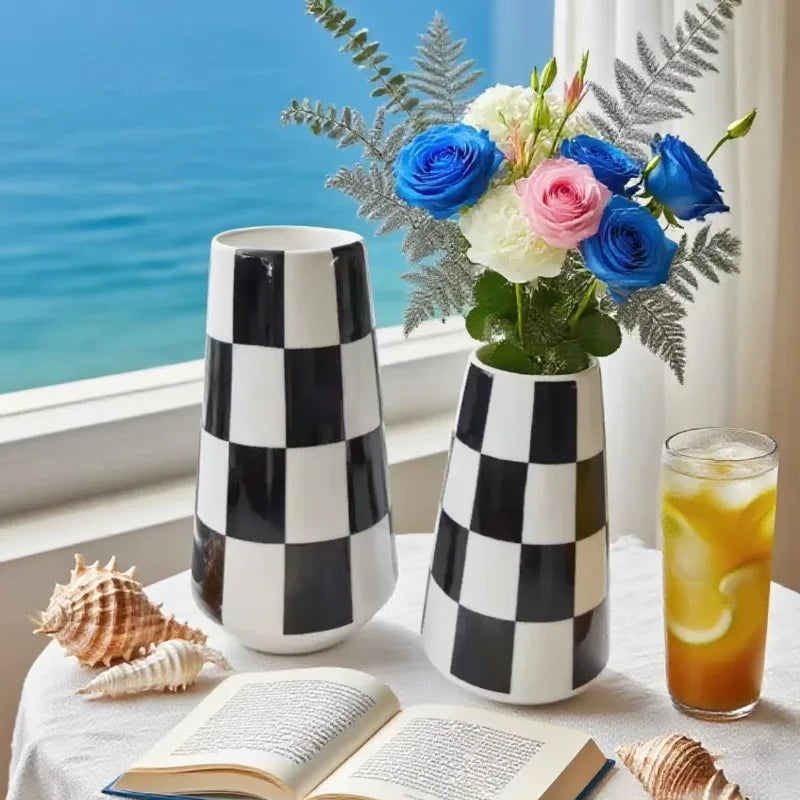 A minimalist black and white checkered ceramic vase holding a bouquet of blue and pink flowers on a table.